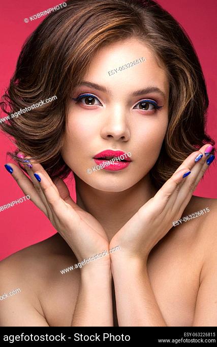 Beautiful model girl with bright makeup and red heart in the hands. Beauty face. Short colorful nails. Picture taken in the studio on a red background