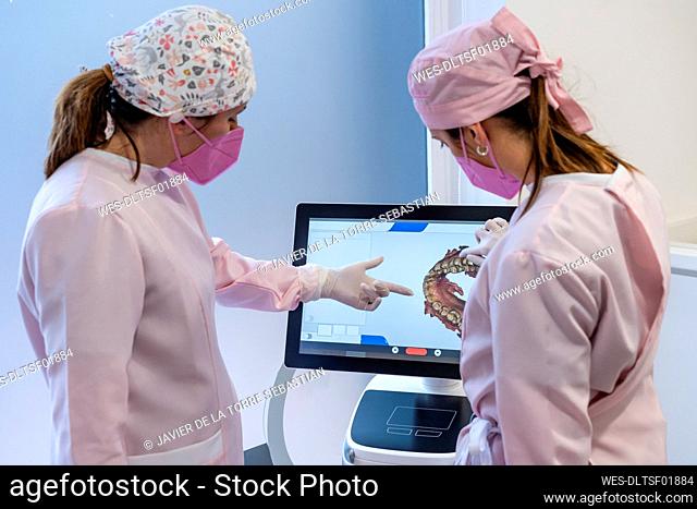 Female dentists in uniform examining digital image of teeth on screen at clinic