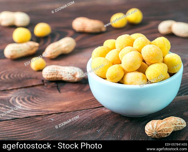 Peanut snack for beer, wine, party bar. Salted peanuts in yellow cheese glaze on brown wooden table. Copy space