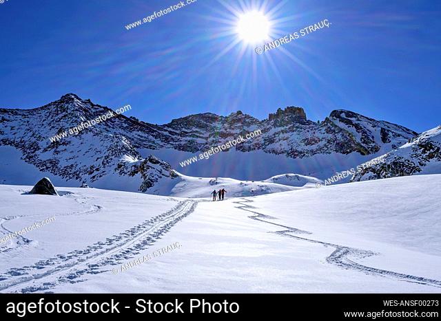 Austria, Tyrol, Sun shining over skiers traveling through snow at Hollensteinkar