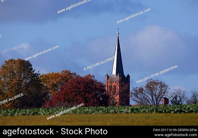 04 November 2020, Brandenburg, Perleberg/Ot Groß Linde: The top of the church tower in Groß Linde can be seen behind a willow and next to autumnally leafy trees