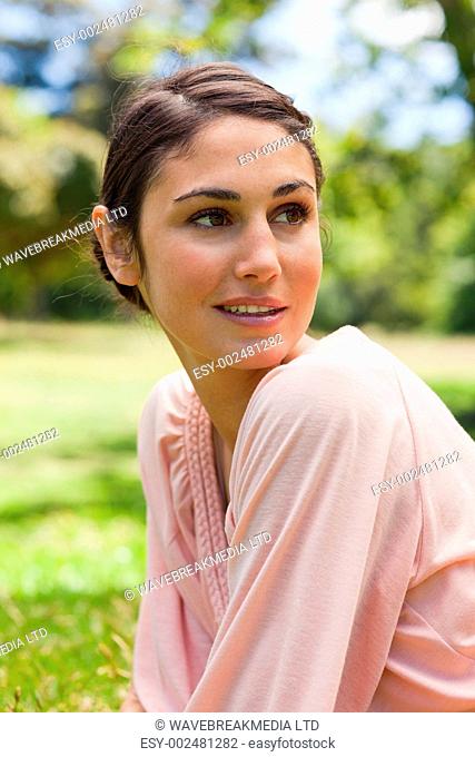 Woman with curious expression on her face looking towards the side as she sits down on the grass