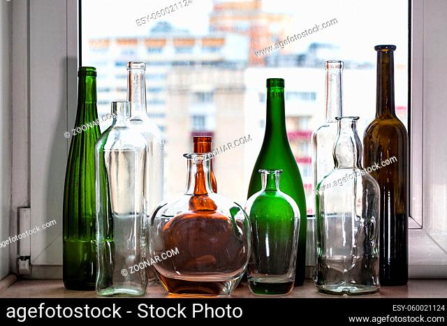 many empty bottles on windowsill and view of city through home window on background