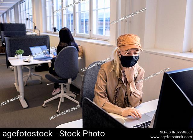 Women in face masks working on laptops in office