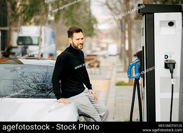 Handsome man with car at electric vehicle charging station
