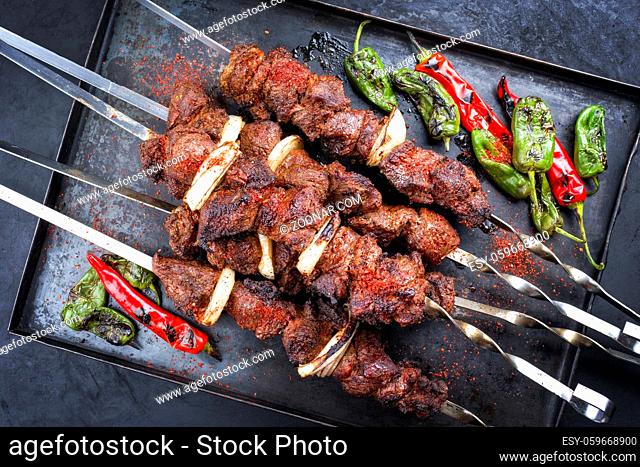 Traditional Russian lamb shashlik on a barbecue skewer with chili, onion and sumach as top view on a rustic metal tray