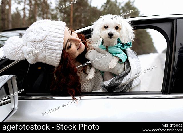 Smiling woman with pet dog leaning out of car window