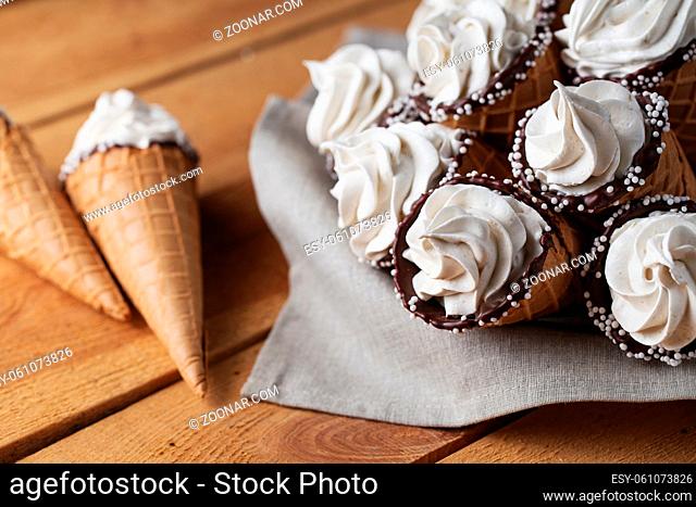 A lot of ice cream cones on wooden table. Soft ice creams or frozen custard in cones. Waffle marshmallow imitating ice cream