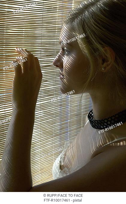 Young woman peering through blinds, side view, close-up