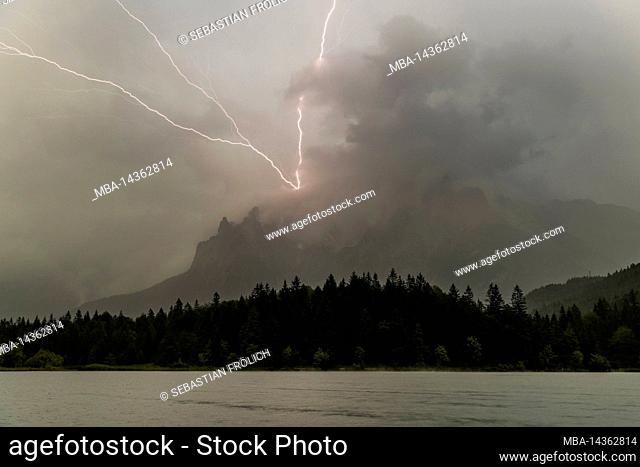 Thunderstorm lightning at the Karwendel above Mittenwald into the western Karwendelspitze. In the foreground the Lautersee and forest