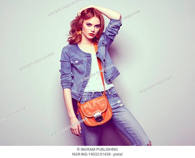 Fashion portrait of beautiful young woman with red hair. Girl in blouse and jeans. Jewelry and hairstyle. Girl with handbag