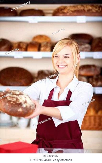 Happy young waitress giving bread while looking away in cafe