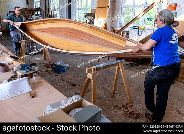 19 May 2022, Mecklenburg-Western Pomerania, Peenemünde: Boat builder Ursula Latus turns the wooden canoe two-seater around together with course participant...