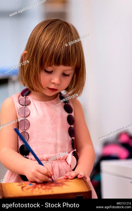 beautiful cute little girl in pink dress painting jewelry box while having fun at home