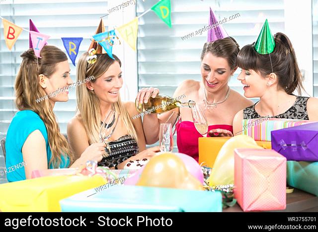 Cheerful woman holding a gift box while looking up overwhelmed by the appreciation of her best friends during a surprise birthday party at home