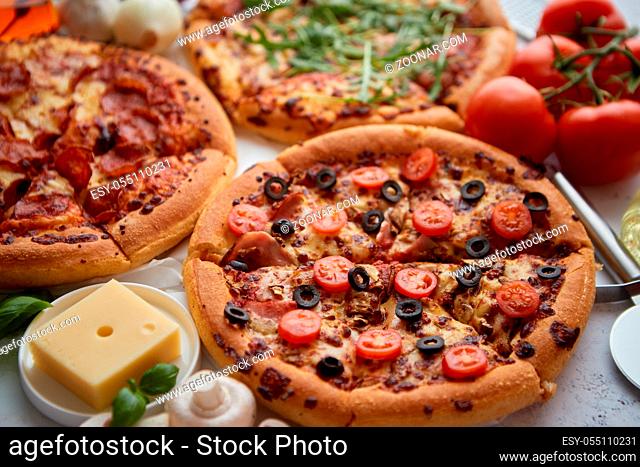 Three american style pizzas with thin fluffy dough served on a table. Placed with various ingredients on side