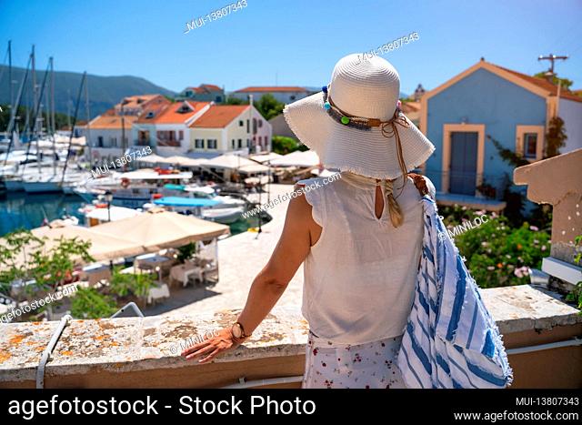 A tourist woman with hat enjoy view of idyllic village of Fiskardo, Kefalonia, Greece, during summer vacation time