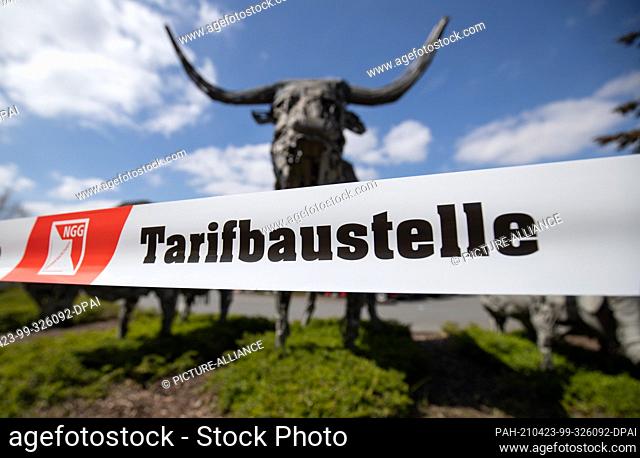 23 April 2021, North Rhine-Westphalia, Rheda-Wiedenbrück: ""Tarifbaustelle"" is written on a ribbon in front of a sculpture of a bull