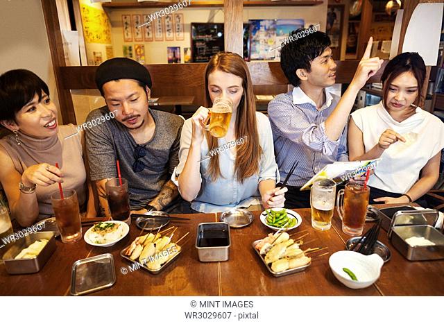 Five people sitting sidy by side at a table in a restaurant, eating and drinking beer