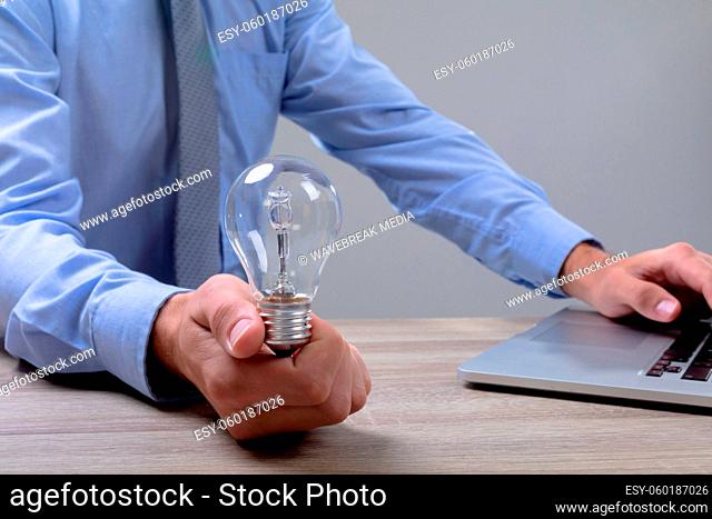 Midsection of caucasian businessman holding light bulb using laptop, isolated on grey background