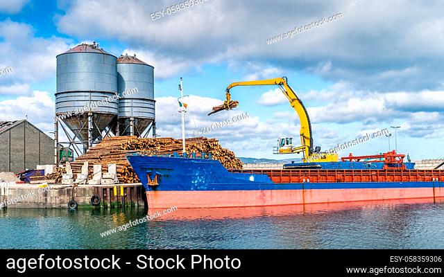 Crane with wood logs gripple loading timber on cargo ship for export in Wicklow commercial port. Transport industry in Ireland