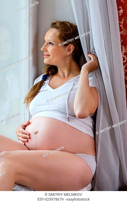Pregnant woman sits near window in the room