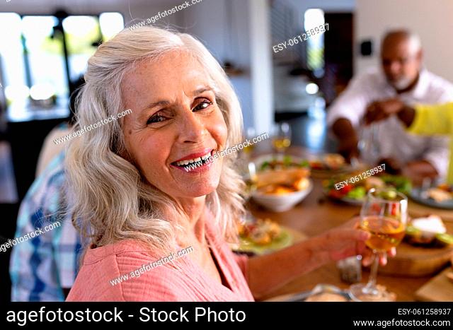 Portrait of senior multiracial woman enjoying wine while having lunch with friends at dining table