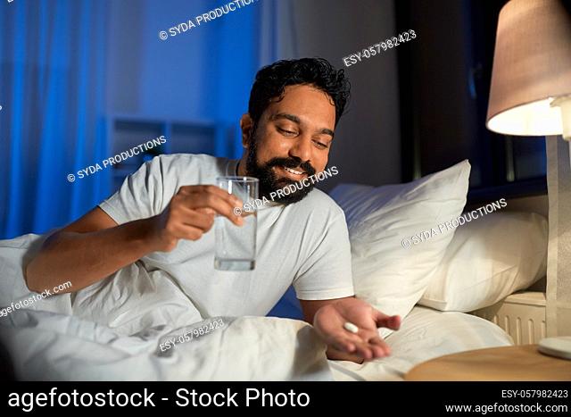 indian man with medicine and water in bed at night