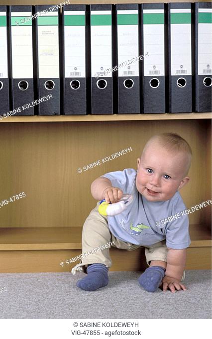 Baby sit in a bookshelf. Symbol picture about single parent, homework. - ERKELENZ, GERMANY, 04/11/2003