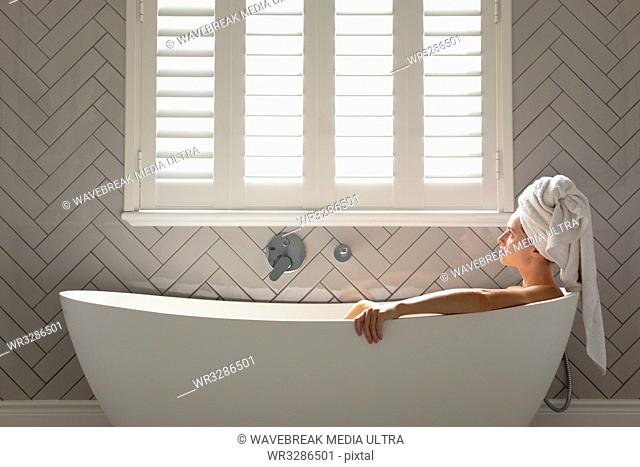 Thoughtful woman sitting in the bathtub in bathroom at home