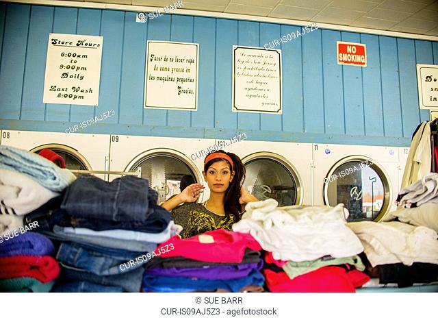 Young woman in laundromat, standing behind piles of laundry