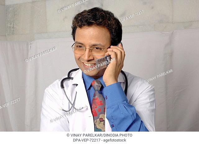 Young Indian Doctor smiling , in white coat , with stethoscope , talking on mobile phone in clinic hospital