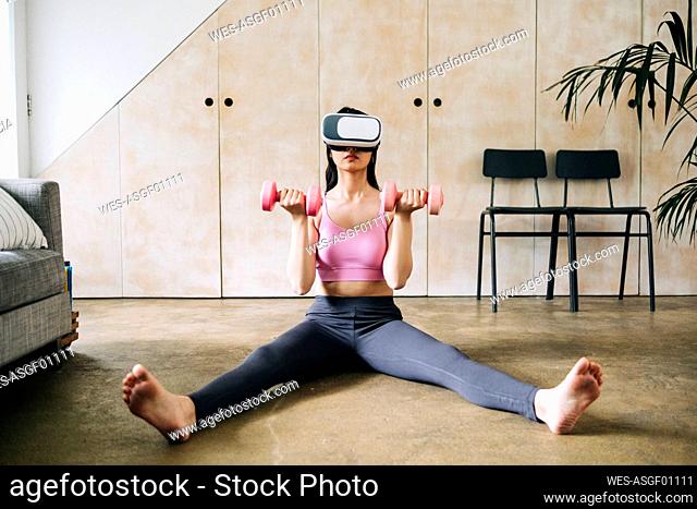 Woman using virtual reality headset while exercising with dumbbells at home