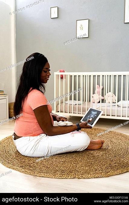 Young pregnant woman watching ultrasound video on digital tablet at home