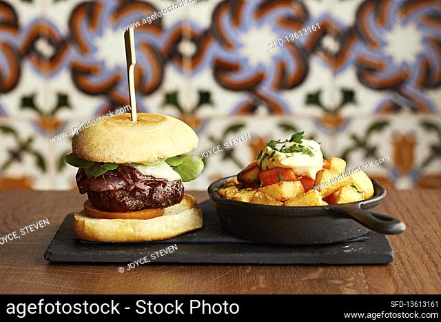 A cheese burger with red onion relish, fried potatoes and aioli in a skillet