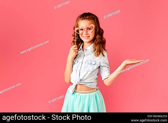 cute little caucasian redhead child girl pointing at empty space on pink background
