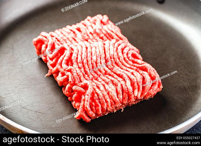 Fresh raw minced beef in frying pan and ingredients over dark background