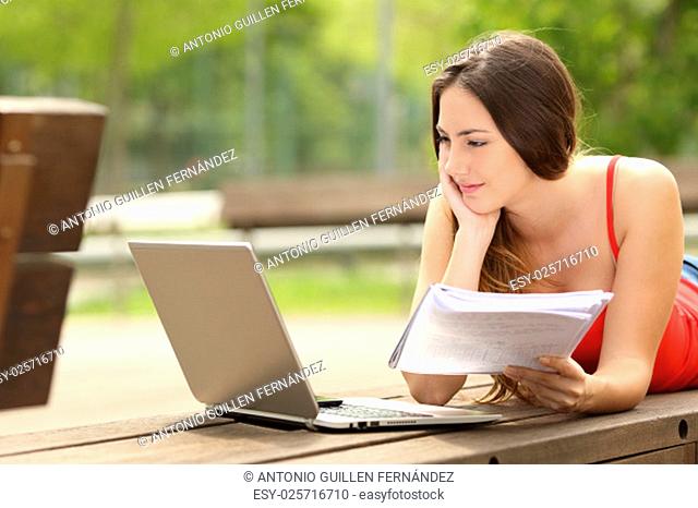 Concentrated student girl studying with a laptop lying in a bench in an university campus