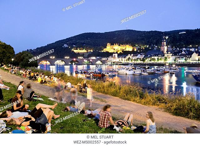Germany, Heidelberg, People on river bank with castle in background