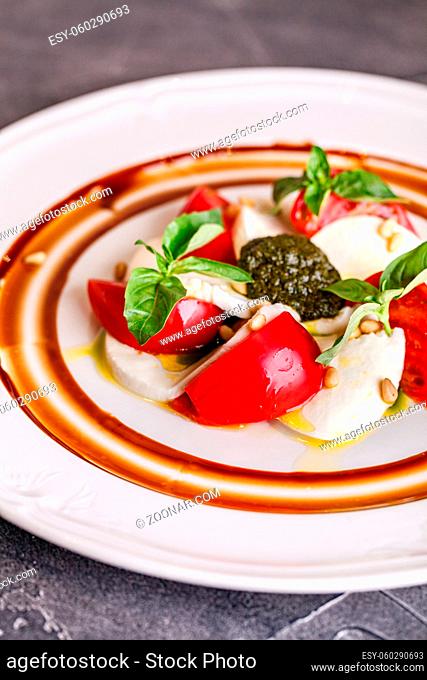 Caprese salad with mozzarella, tomato, basil and pesto arranged on white plate