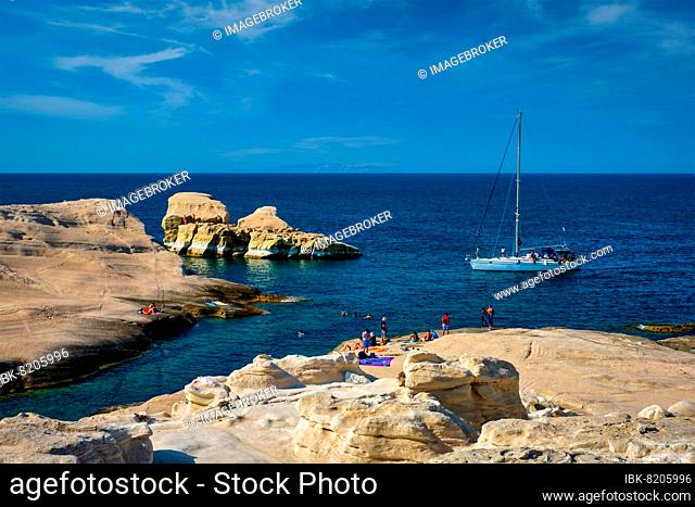 Yacht boat at famous Sarakiniko beach white rocks tourist attraction with tourists on beach in Aegean sea on sunset, Milos island, Greece, Europe