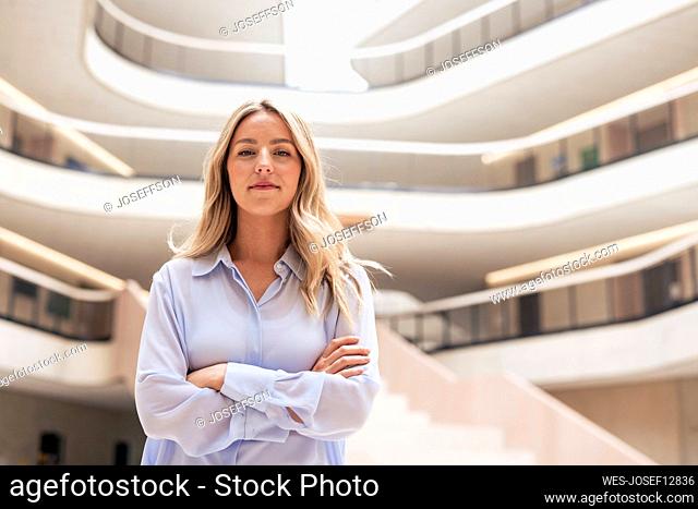 Confident blond businesswoman with arms crossed in lobby
