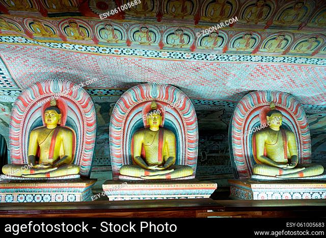 Group of sitting Buddha statues in cave buddhist temple with bright painted murals on walls and ceiling in Dambulla Golden temple in Sri Lanka