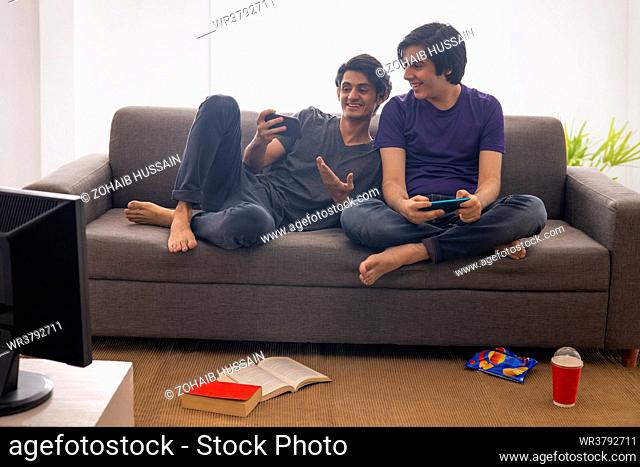 Two teenage boys playing video games on smartphones in living room