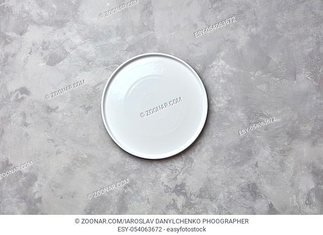 Porcelain handmade empty round a plate on a gray concrete background with a copy of space. Can be used for display or montage your products. Flat lay