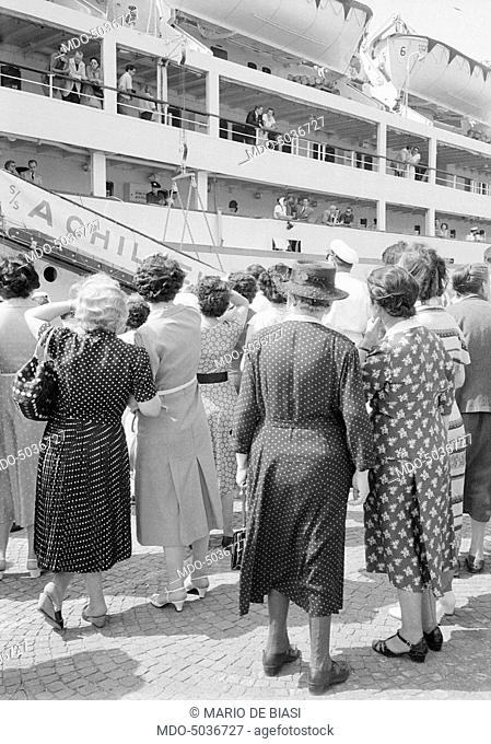 Curious people watching VIP guests getting on the Achilleus yacht for a cruise, during the XVI Venice International Film Festival. Venice, 1955