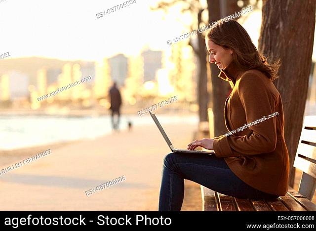 Profile of woman using laptop sitting on a bench in winter in a park in a beach town