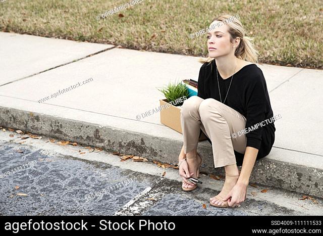 Distraught employee sitting on the curb with a box of her belongings