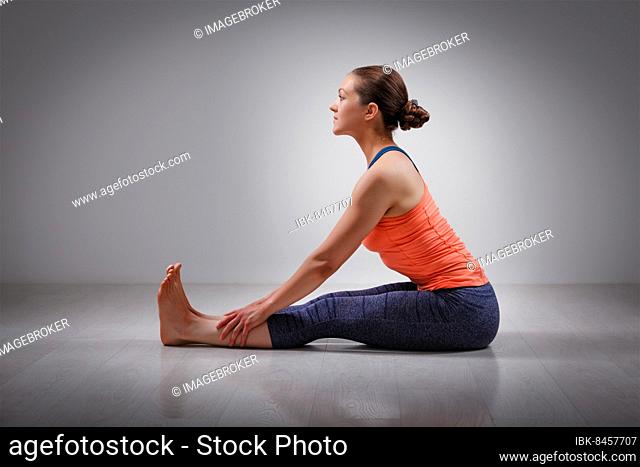 Sporty fit woman practices Ashtanga Vinyasa yoga back bending asana Paschimottanasana, seated forward bend beginner variation
