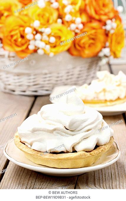 Pavlova cake filled with peach jam, bouquet of orange roses in the background